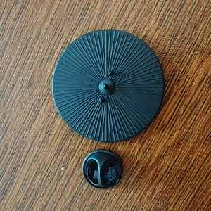 Detail of a matte black alloy pin back with butterfly clasp on a brown wood surface