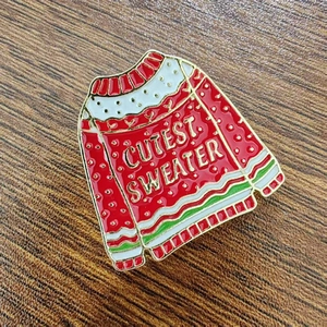 Detail of red enamel Christmas sweater brooch pin with Cutest Sweater text engraving