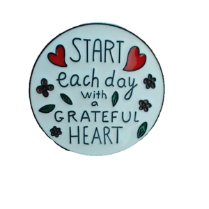 Round enamel badge with Start Each Day With a Grateful Heart text and floral motifs