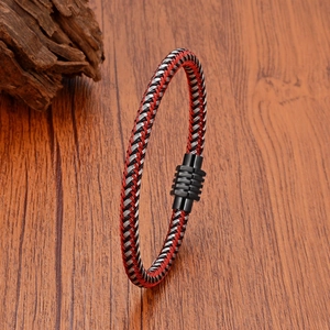 Detail of red and black braided leather bracelet with a magnetic metal clasp on wood
