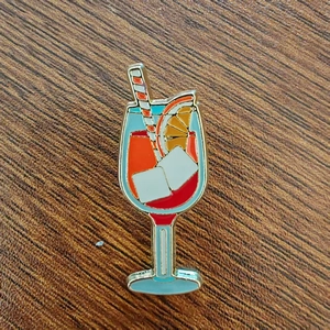 Vibrant cocktail glass enamel pin with orange slice detail on wooden background