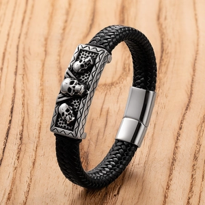 Men's punk woven leather bracelet with silver skull charms and magnetic clasp on wood