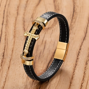 Dettaglio di bracciale in pelle nera con pendente a croce dorata e cuciture bianche