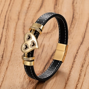 Detail eines schwarzen Leder-Armbands mit goldenem Herzanhänger und Magnetverschluss