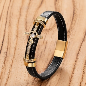 Detail of black leather bracelet with gold cross and heart charm on wood background