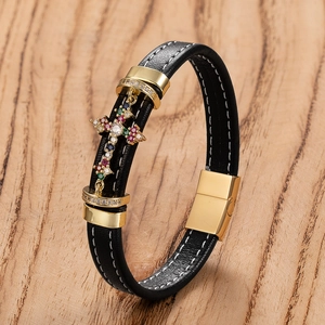 Men's woven black leather bracelet with gold cross pendant and magnetic clasp on wood