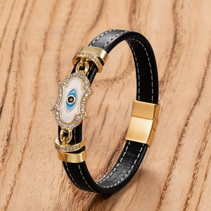 Detail von schwarzem Lederarmband mit goldener Hand der Fatima und Nazar-Auge auf Holz