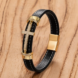 Detail view of black braided leather bracelet with golden zircon-studded cross on wood base