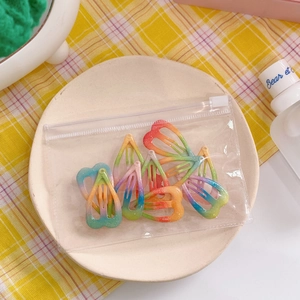 Detailed macro of glittery rainbow gradient star and heart hair clips in a small storage bag