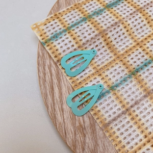 Detail of two mint green heart-shaped cutout drop hair clips on a wooden tray