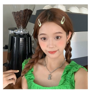 Détail d'une fille portant une barrette à fleurs verte et un collier à pendentif ours
