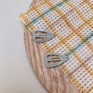 Close-up of small heart-shaped matte grey hair clips on a wooden tray with mesh fabric