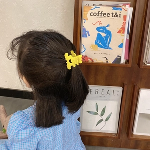 Détail d'une pince à cheveux fleur jaune mat sur cheveux foncés pour un look quotidien
