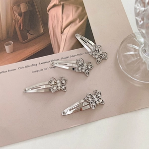 Close-up of four silver butterfly hair clips with sparkling rhinestones on a beige background