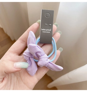 Détail d'un nœud en lin lavande et d'un élastique à cheveux bleu sur un fond doux