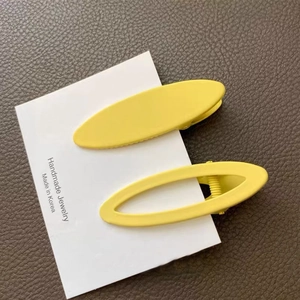 Close-up of yellow oval matte hair clips on a white card over dark brown leather