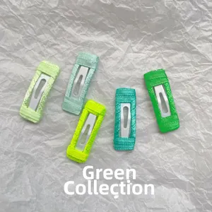 Detail showing five assorted green fabric wrapped 3cm square BB hair clips for dogs