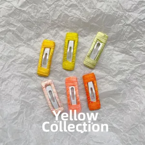 Detail of six handmade yellow embroidered rectangular snap hair clips on white paper