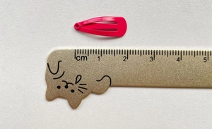 Macro d'une mini pince à cheveux rose de 2cm à côté d'une règle pour montrer la taille