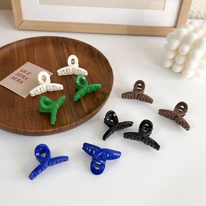Close-up of nine mini glossy hair claws in blue, green, and black on a wooden tray