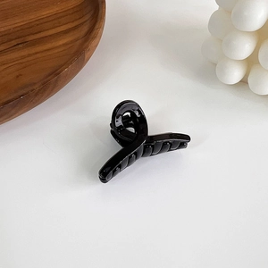 Close-up of minimalist black glossy shark hair claw clip with crossed design on white surface