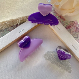 Detail of three heart-shaped purple acetate hair claws on a decorative soft background