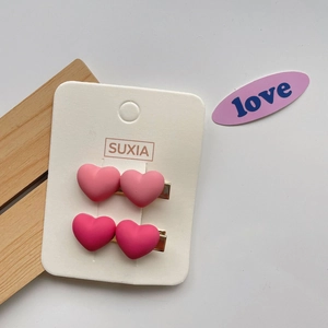 Close-up of pink heart-shaped hair clips in matte finish on a white display card