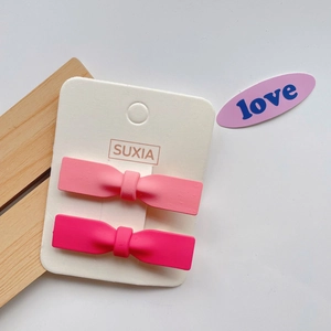 Close-up of pink bow hair clips on branded card with matte finish and wooden decor