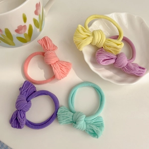 Five macaron-colored elastic bow hair ties in pink, purple, and mint green on a tray