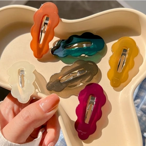 Close-up of six colorful wavy hair clips in warm autumn tones on a ceramic tray