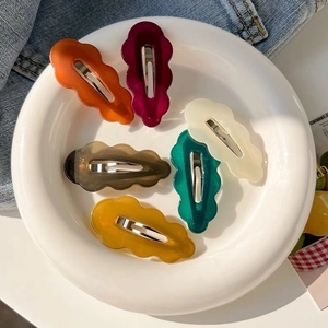 Set of six colorful wavy acrylic hair clips in autumn tones on a white ceramic plate
