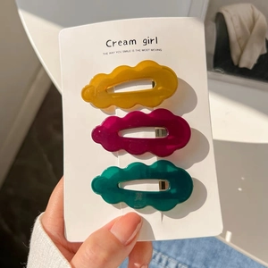 Close-up of wavy acrylic hair clips in yellow, red, and green on Cream Girl card