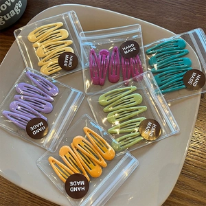 Detail of candy color metal hair clips set in transparent packaging bags on a ceramic plate