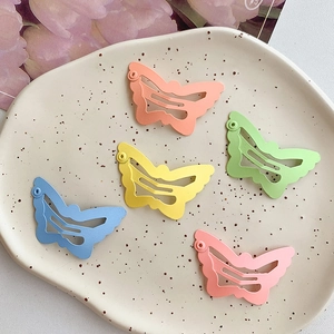 Five colorful butterfly metal hair clips in macaron shades on a ceramic tray