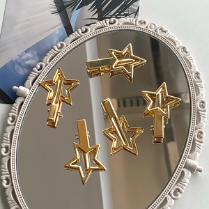 Close-up of five golden star-shaped metal hair clips on a decorative mirror surface