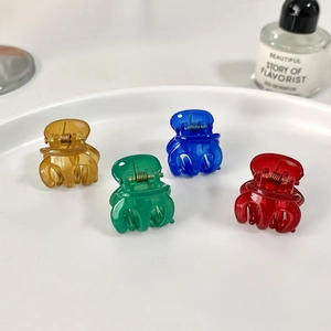 Small candy-colored pumpkin hair claws in yellow, green, blue, and red on a white tray