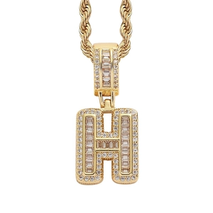 Macro detail of iced-out gold H pendant featuring baguette and round cubic zirconia