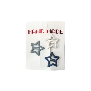 Three matte star hair clips in grey, blue, and white colors on a handmade card display