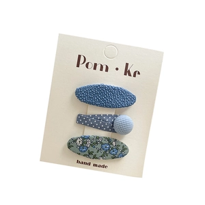 Three-piece set of blue fabric hair clips featuring bow, lace, and floral patterns on card