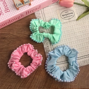 Three-piece set of pastel pearl scrunchies in pink, mint green and blue on wooden desk