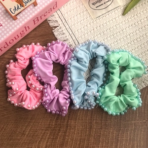 Set of four pastel pearl scrunchies in pink, purple, blue and green on a wooden desk