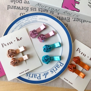 Lot de jolies barrettes roses en cuir métallisé coloré présentées sur une assiette fleurie