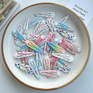 Close-up of colorful metal BB hair clips with polka dots and stars pattern in a white bowl