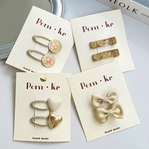 Lot de barrettes à cheveux avec cœur pailleté et nœud en doré et crème sur présentoir
