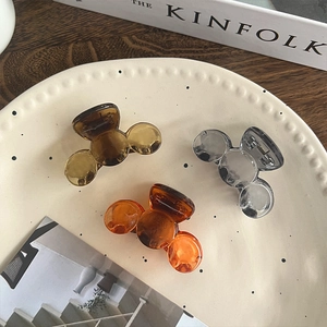 Three translucent mini hair claws in amber, orange, and smoke grey on a ceramic plate