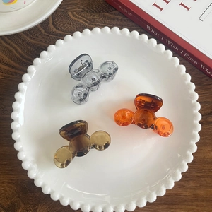 Three-piece set of mini translucent hair clips in amber and grey on a ceramic plate