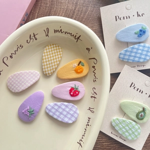 Detailed macro of embroidered fabric fruit hair clips and colorful plaid BB clips set