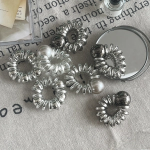 Détail d'élastiques spirales argentés avec perles et billes métalliques sur tissu