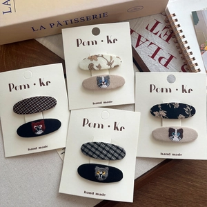 Détail de barrettes brodées chat avec motifs à carreaux et fleurs sur emballage