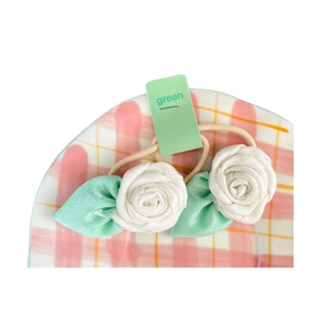 Minimalist white rose flower hair ties with green leaves on a checkered plate